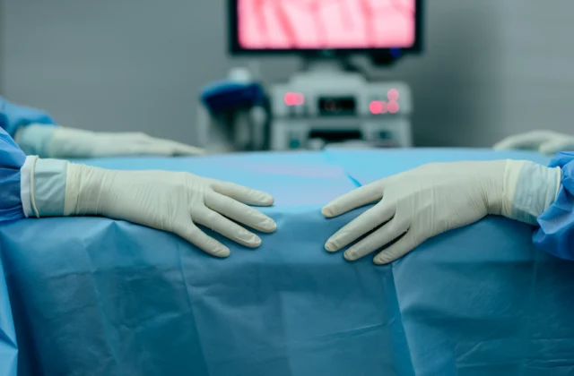 Χέρια χειρουργού με γάντια στο χειρουργείο κατά την αρθροσκόπηση ισχίου, με οθόνη στο βάθος